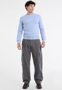 Světle modrá mikina s kulatým výstřihem a vyšívaným logem "Guess Jeans", spárovaná se šedými cargo kalhotami s bočními kapsami.
