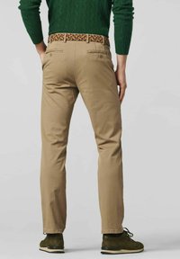 Tan chinos with a straight fit, featuring back pockets and a multicolored braided belt. Styled with dark green sweater and dark shoes.