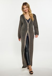 Cardigan lungo aperto in maglia nera metallizzata con maniche lunghe e dettagli con bottoni, abbinato a un top blu navy e leggings neri.