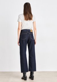 Mörkblå vida jeans med hög midja, bakfickor och en tan läderlapp vid midjan. Bärs med en grå T-shirt och svarta stövlar.