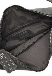 Interno di una borsa a tracolla in pelle nera caratterizzato da una superficie liscia, una tasca con zip e un'etichetta con il logo. La fodera è scura e opaca.