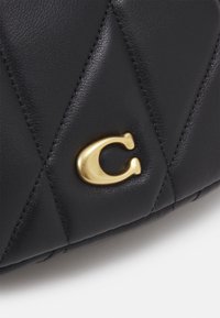 Surface en cuir matelassé noir avec une lettre métallique dorée en relief "C" fixée près de motifs de losanges cousus.
