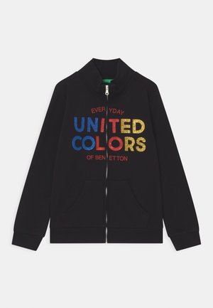 Sort lynlåstrøje med blå, rødt og gult "United Colors of Benetton"-tekst og forlommer, lagt fladt på en hvid baggrund.