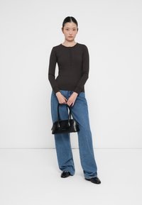 Bruine geribde langwerpige top met knoopdetails, gecombineerd met lichtblauwe wijde jeans. Zwarte handtas met ronde randen en handvatten.
