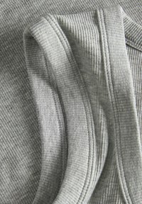 Tessuto grigio con texture che presenta motivi rigati e bordi lisci in contrasto. Materiale morbido con dettagli di cucitura visibili.