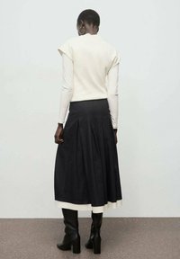 Haut blanc à manches courtes associé à une longue jupe noire avec des plis et un ourlet blanc. Modèle portant des bottes noires jusque-aux-genoux.