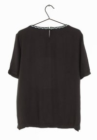 Svart blus med kort ärm och rund halsringning. Har en flätad kant i ljusblått vid halsen och en liten nyckelhålsöppning bak.