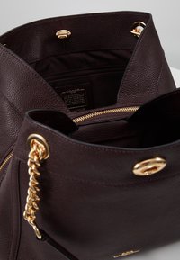 Bordowa torba typu tote z skóry z złotymi elementami, grubym łańcuchem, zapięciem na zamek oraz pojemnym wnętrzem z jedną kieszenią.