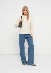 Cream knitted sweater with a high neckline, paired with wide-leg blue denim jeans. Accessorized with a small dark handbag.