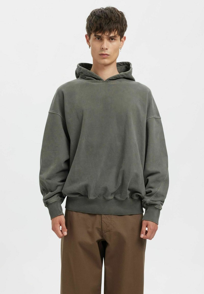 Přehnaně velká šedá mikina z měkké látky s kapucí na stažení, žebrovanými manžetami a lemem, zkombinovaná s hnědými kalhotami. Jednoduchý, uvolněný design.