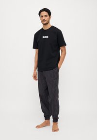 Must musta T-särk "BOSS" logo'ga, millele on paaritatud mustad triibulised pidžaamapüksid, millel on multivärvilised vertikaalsed jooned ja elastsed mansetid.