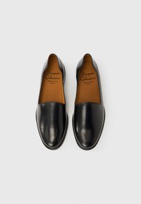 Μαύρα δερμάτινα παπούτσια τύπου slip-on με λεία υφή, στρογγυλεμένη μύτη και ταμπά πάτο με τυπωμένες λεπτομέρειες της μάρκας. Απλός, κλασικός σχεδιασμός.