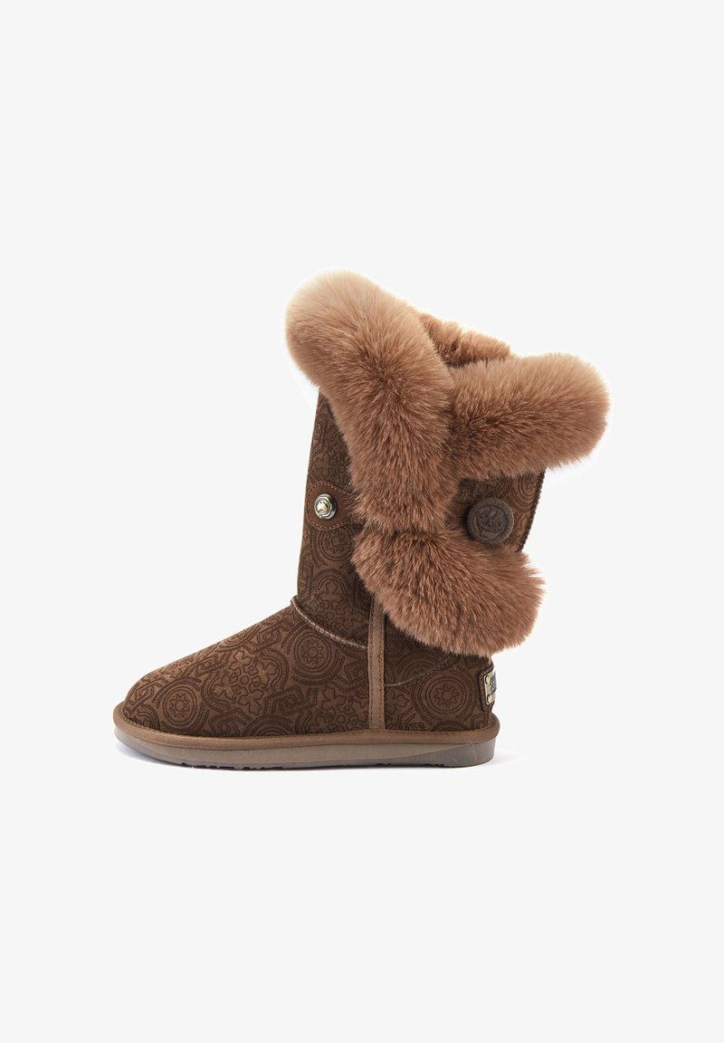 Hnedé čižmy podšité kožušinou s ozdobným vzorom na povrchu, so širokým kožušinovým lemom a dekoratívnym gombíkom na boku. Ploché gumené podrážky.