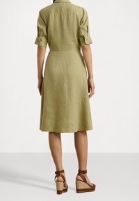Ljus olivgrön linnekjol med korta ärmar, åtsittande midja och utsvängd kjol. Bärs med bruna klacksandaler med remmar.