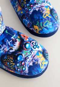 Krāsaini spēļu tematiskie klumpi ar zilu auduma augšdaļu, kas rotāta ar dzīvespriecīgu grafiku kolāžu, tostarp spēļu kontrolieru motīviem un grafiti akcentiem.