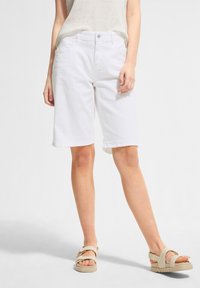 Valkoiset puuvillashortsit suoran lahkeen suunnittelulla, joissa on napin suljenta ja etutaskut. Yhdistetty vaaleanbeigeihin sandaaleihin.