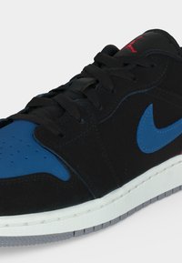 Μαύρο και μπλε παπούτσι Nike Air Jordan με μαύρα κορδόνια, μπλε λογότυπο Swoosh, κόκκινο λογότυπο Jumpman στη γλώσσα και λευκή σόλα.