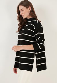 Pulover cu dungi alb-negru, cu guler înalt, accente cu nasturi pe laterale și croială lejeră. Fabricat dintr-un material moale, cu o siluetă relaxată.