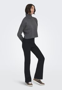 Maglione grigio a collo alto corto, pantaloni neri svasati e sneaker marroni con strisce bianche. Il maglione ha una consistenza morbida e un fit rilassato.