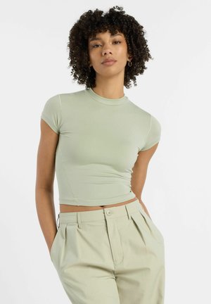 Lysgrøn, tætsiddende crop top med korte ærmer og høj hals, lavet af glat stof. Sammen med lyse, plisserede bukser.