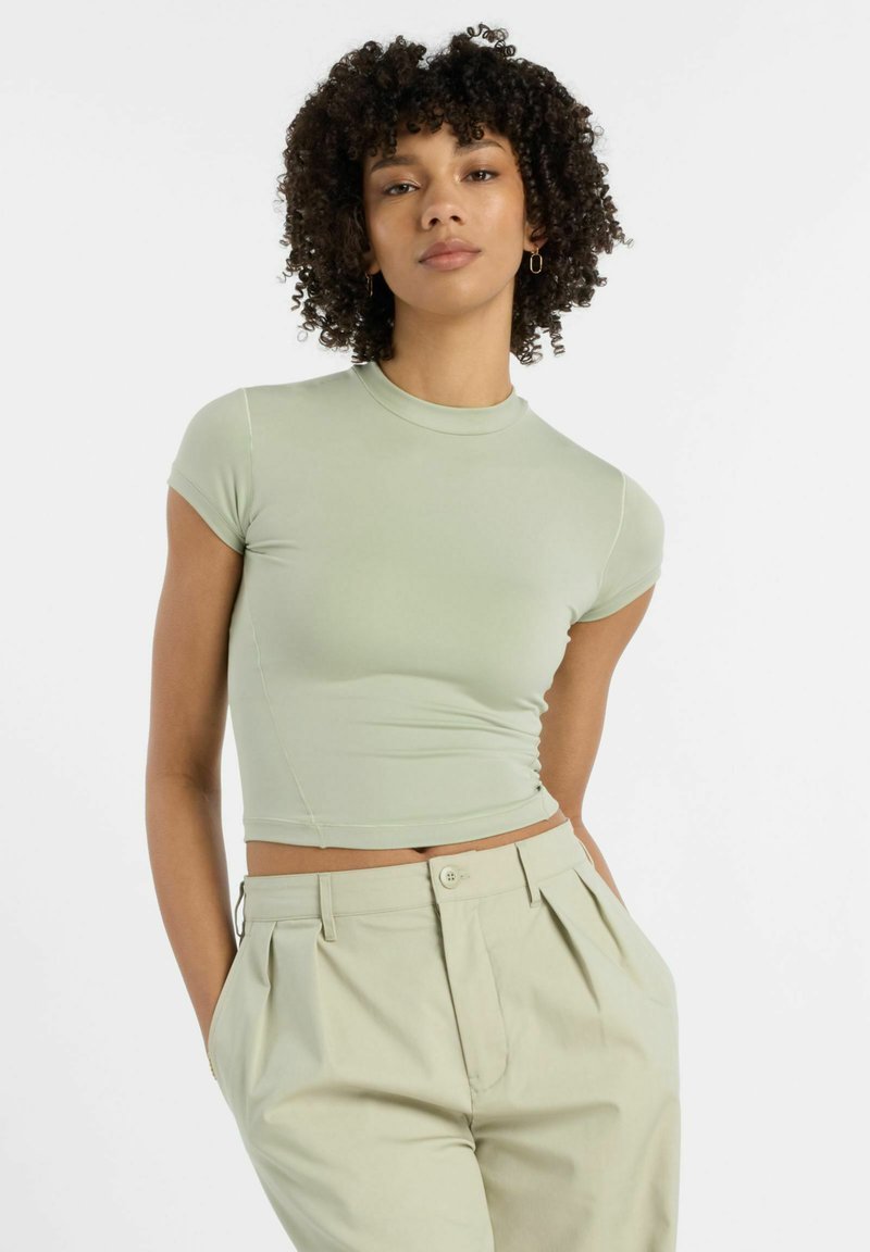 Lysgrøn, tætsiddende crop top med korte ærmer og høj hals, lavet af glat stof. Sammen med lyse, plisserede bukser.