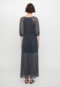 Robe longue bleu marine en tissu transparent avec des motifs floraux blancs. Caractérisée par une taille cintrée, des manches bouffantes et une silhouette fluide.