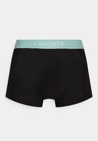 Fekete boxer alsónemű világoskék gumírozott derékkal, amelyen a "LACOSTE" logó található. Sima anyag, testhezálló fazon, minimális varrási részletekkel.