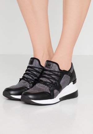 Pair of black and metallic gray wedge sneakers with laces worn on feet against a light gray background.