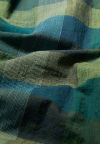 Cotton fabric with a plaid pattern in dark green, teal, and yellow. Textured surface with a soft drape and varying stripe widths.