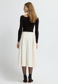 Un haut noir côtelé à manches longues associé à une jupe midi plissée blanche. Des bottes chelsea en daim marron et des chaussettes sombres complètent l'ensemble.
