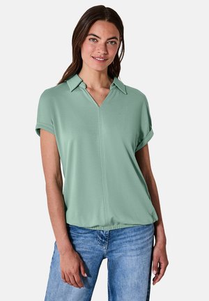 Polo shirt vert clair à manches courtes, col en V et manches retroussées. Fabriqué en tissu lisse avec une coupe décontractée.