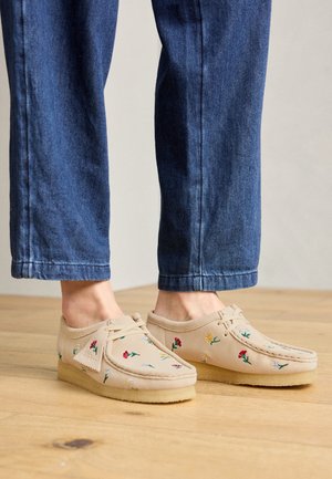 Beige mokkasinstøvler med flerfarvet blomsterbroderi, båret med cropped blå jeans på trægulv.