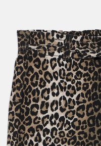 Leopardmönstrad tyg med olika nyanser av tan och svart. Utformad med midjeband och bältesöglor, vilket visar en strukturerad yta.