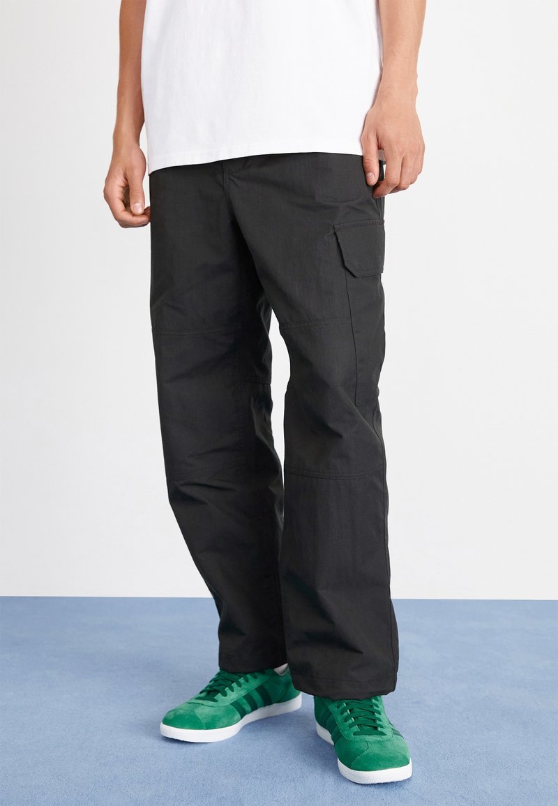 Zwarte cargobroek met een rechte pasvorm, voorzien van zijzakken en een gladde textuur. Gecombineerd met groene sneakers. Eenvoudig wit T-shirt erboven.