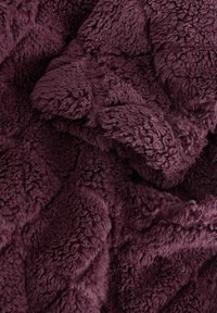 Dybt lilla blødt plysstof med en tekstureret, fluffy overflade, der har folder og krusninger.