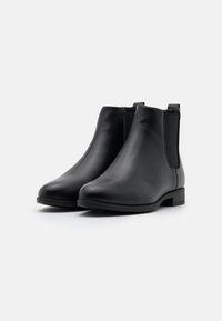 Bottines Chelsea en cuir noir avec panneaux élastiques sur les côtés et petit talon empilé. Texture lisse et design à bout rond pour un style facile à enfiler.