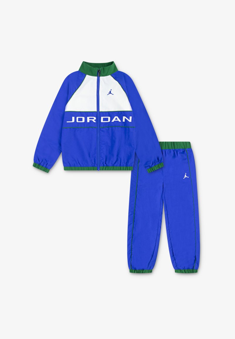 Μπλε αθλητική φόρμα φτιαγμένη από ελαφρύ υλικό. Η ζακέτα διαθέτει λευκές και πράσινες λεπτομέρειες με το κείμενο "JORDAN". Τα παντελόνια έχουν ελαστικές μανσέτες και λογότυπο.
