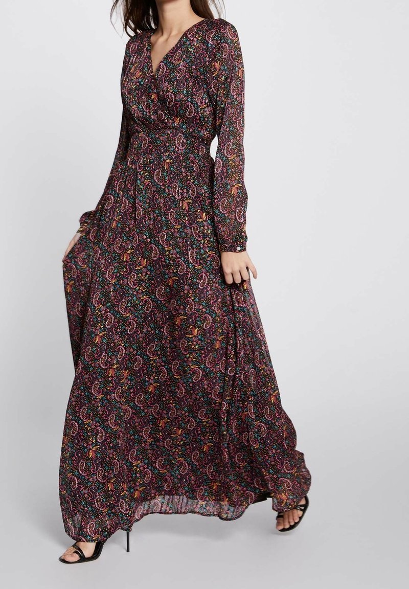 Femme portant une robe noire longue à manches longues avec un motif cachemire coloré et des sandales noires à talons ouverts.