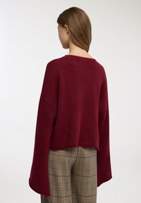 Maglione bordeaux lavorato a maglia con maniche larghe, design leggermente corto e finitura testurizzata, abbinato a pantaloni a quadri con una combinazione di colori tenue.