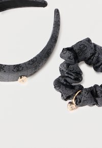 Το σετ περιλαμβάνει μια μαύρη υφασμάτινη κορδέλα κεφαλής με ένα γοητευτικό καρδιάς και μια αντίστοιχη ελαστική ταινία με μικρή λεπτομέρεια καρδιάς. Και τα δύο έχουν υφή επιφάνειας.