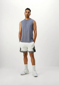 Hall halli ilman varrukaita oleva tipp-logo, valged lühikesed püksid mustade aktsentidega ja külgtriipudega, valged sokid ning valged tossud. Lihtne sportlik disain.