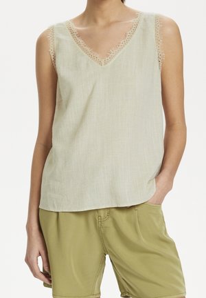 Top senza maniche di un beige chiaro con bordi in pizzo lungo il collo a V e le aperture per le braccia, realizzato in un tessuto testurizzato. Abbinato a pantaloni shorts verdi oliva.