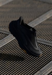 Chaussure noire à enfiler avec un dessus texturé, fermeture éclair et semelle en caoutchouc. Comprend un logo bien visible sur le côté et un design durable et léger.