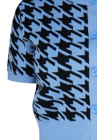 Rövidujjú kardigán világoskék kötött anyagból, fekete houndstooth mintával. Kerek nyakkal és gombos záródással rendelkezik. Puha tapintású.