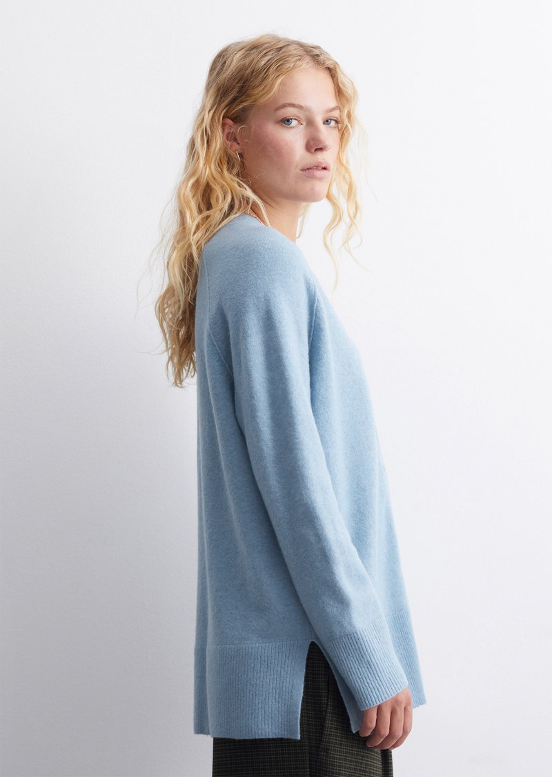 Hellblauer gestrickter Pullover mit langen Ärmeln, gerippten Bündchen und einem seitlichen Schlitz am Saum für zusätzliche Textur und Form. Lässiges Design.
