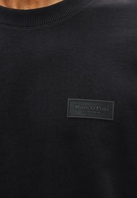 Μαύρη μπλούζα φούτερ με ριγωτό λαιμόκοψη, διαθέτει υφασμένο μαύρο ταμπελάκι με τη λέξη "Marc O'Polo" αποτυπωμένη στην αριστερή περιοχή του στήθους.