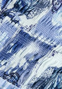 Tissu texturé dans des nuances de bleu et de blanc, avec des sections froncées et un motif floral, créant une apparence ondulée.