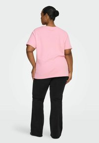 Różowy bawełniany T-shirt z krótkim rękawem, okrągłym dekoltem i luźnym krojem, zestawiony z czarnymi dzwonowatymi spodniami dżinsowymi o gładkiej fakturze.