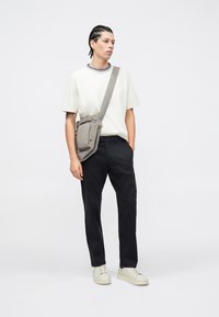 Szara torba listonoszka noszona przez ciało na białej koszulce z niebiesko-białym kołnierzykiem, zestawiona z ciemnymi spodniami i białymi trampkami.