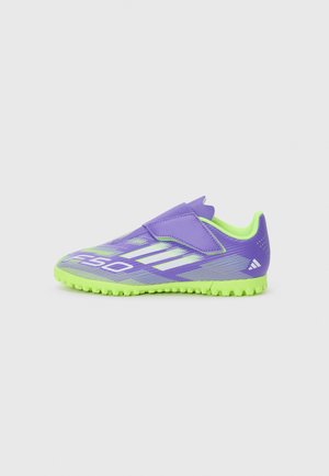 Lila Sportschuh mit einer neongrünen Sohle, ausgestattet mit einem Klettverschluss, strukturiertem Obermaterial und diagonalen weißen Streifen als Designelement.